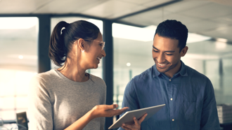 Two people smiling while one looks at a tablet the other person is holding