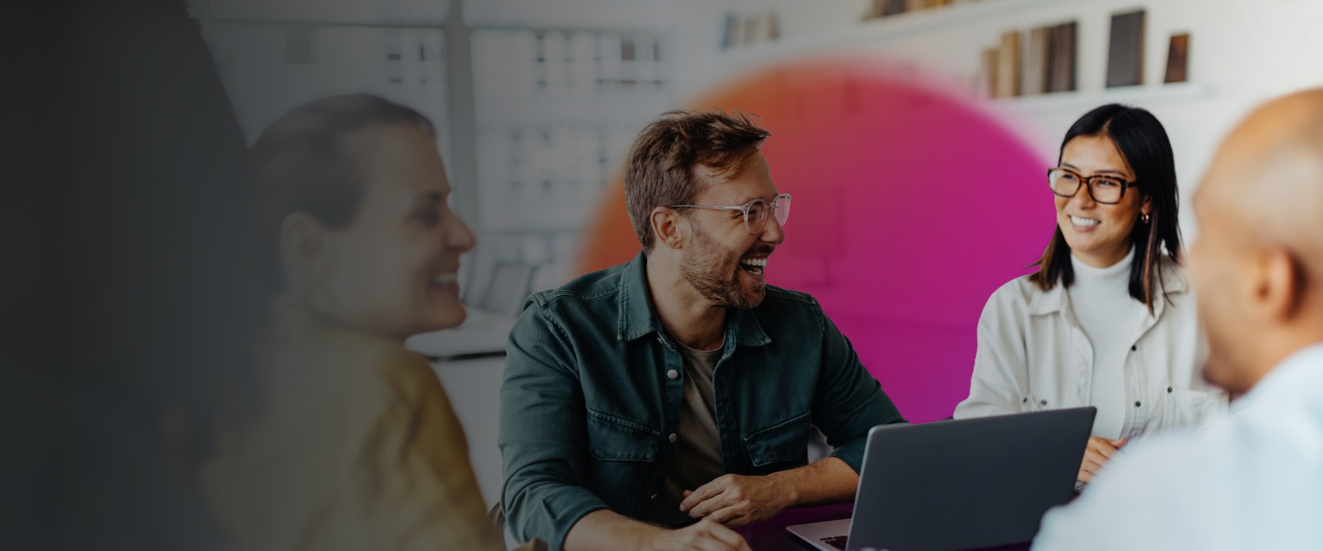 Several coworkers in a room laughing with a orange and pink circle in the background