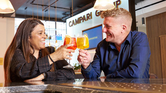 Two individuals smiling while enjoying a toast with drinks in their hands