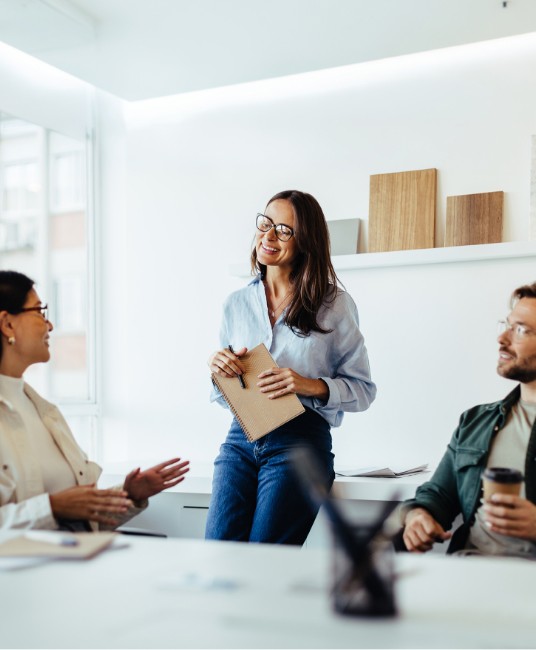 Woman talking in a meeting smiling and holding a notebook