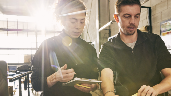 A female and male coworkers chatting over a clipboard
