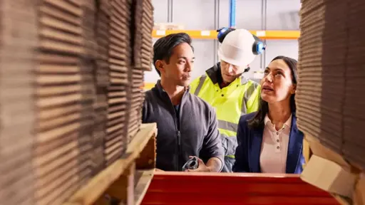 Looking at three people in warehouse through stacks of cardboard boxes