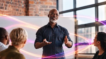 individual standing in front of a whiteboard, speaking to a group of people